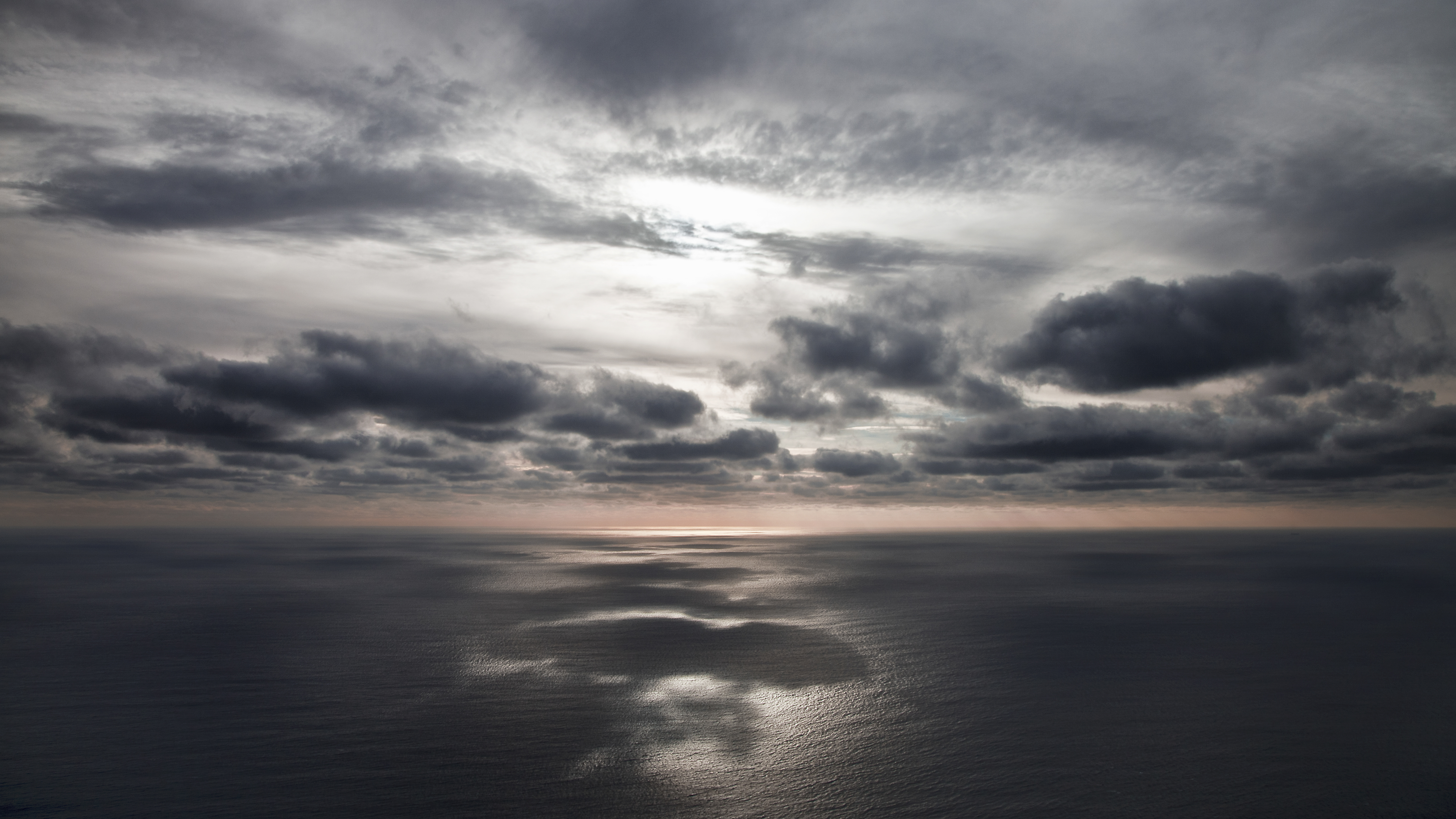 A distant sunset ocean horizon, dark clouds reflecting on the sea.